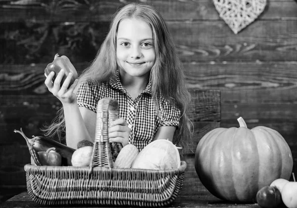 Kid girl near basket full of fresh vegetables harvest rustic style. Farm market fall harvest. Child girl presenting harvest of her vegetable garden on wooden background. Harvest festival concept