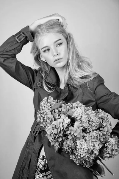Girl fashion model wear coat for spring and autumn season. Trench coat fashion trend. Fashionable coat. Must have concept. Clothes and accessory. Woman blonde hair posing coat with flowers bouquet — Stock Photo, Image