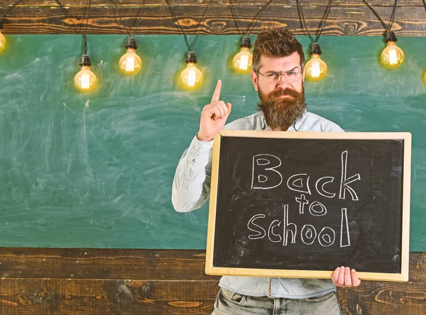 Geri okul kavramı. Sakallı ve bıyıklı sıkı yüzündeki uyardı öğrenciler, kara tahta arka plan. Gözlük öğretmen blackboard yazıt ile geri okula tutar — Stok fotoğraf