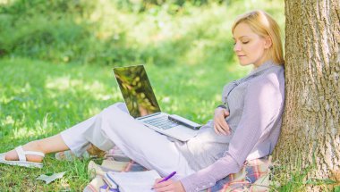 Eğitim teknolojisi ve internet konsepti. Parkta laptop ile kız çalışması çim üzerinde oturmak. Doğal çevre ofisi. Çalışma açık havada faydaları. Kadın dizüstü bilgisayar çalışma açık havada ağaç gövde üzerinde yalın
