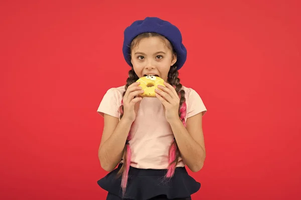 Heerlijke zoete donut. Meisje in baret hoed houden donut rode achtergrond. Kind speels meisje eet donut. Gezondheid en voeding concept. Zoete leven. Snoepjes winkel en bakkerij concept. Kind fan van gebakken donuts — Stockfoto