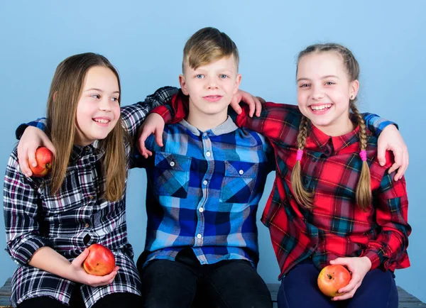 Healthy lifestyle. Boy and girls friends in similar checkered clothes eat apple. Teens with healthy snack. Healthy dieting and vitamin nutrition. Eat fruit and be healthy. Friends kids hug each other