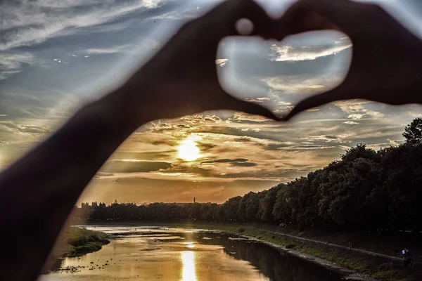 Sunset sunlight romantic atmosphere. Heart gesture in front of sunset above river. Hands in heart shape gesture symbol of love and romance. Romantic date ideas. Idea honeymoon travel. Vacation resort