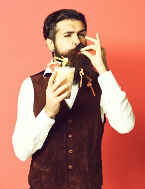 uzun sakallı ve bıyıklı yakışıklı sakallı adam kırmızı stüdyo backgroun üzerinde vintage süet deri yelek alkollü içecek cam tutan komik yüzünde şık saçları vardır