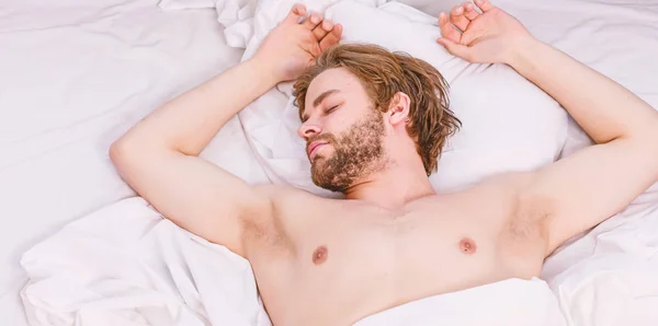 Imagen que muestra a un joven estirándose en la cama. Joven estirándose mientras se despierta por la mañana. El hombre con los ojos todavía cerrados botón de alcance en el reloj para apagarlo . —  Fotos de Stock