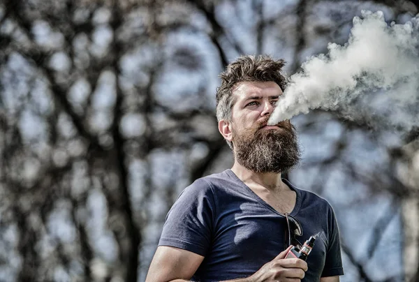 Concepto de alivio del estrés. Hombre barbudo fumando vapor. Fumar cigarrillo electrónico. Hombre barba larga relajado con hábito de fumar. El hombre con barba y bigote exhala humo. Nubes blancas de humo aromatizado — Foto de Stock