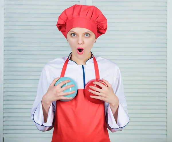 good food for good health. cook in restaurant, uniform. girl in apron and hat hold bowls. professional chef cooking in kitchen. surprised woman loves eating food. tableware choice. culinary cuisine