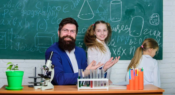 魅惑的な生物学のレッスン。生物学の学校の先生。あごひげを生やした教師は、生物学の教室で顕微鏡と試験管を使って作業します。子どもの興味を持つ方法勉強。子どもたちに生物学を説明する — ストック写真