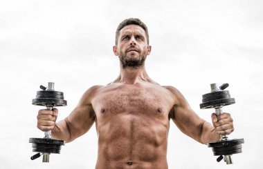 Halter egzersiz salonu. Dambılla egzersiz icra eden kaslı bir adam. Büyüklüğün bedeli sorumluluktur. Güçlü gövdeli sporcu. Spor aletleri. Fitness ve vücut geliştirme sporu. Spor salonu egzersiz konsepti