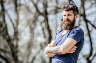 Erkeklik ve erkeklik. Açık havada poz veren çekici sakallı hippi. Yakışıklı bir adamın kendinden emin duruşu. Uzun sakallı, erkeksi görünümlü bir adam. Berber konsepti. Sakal bakımı. Sakal bakımı