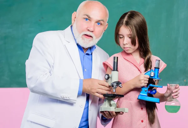 Chemical industry. mature teacher of biology. Pupil girl in school lab. small girl with man tutor study chemistry. use magnifying glass. science classroom. Microscopy. Laboratory equipment