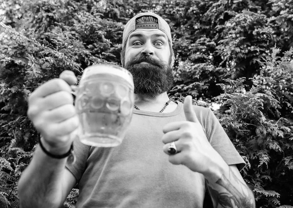 Thumbs up to the best beer. Man drinker holding beer mug. Bearded man enjoy drinking beer on nature. Brutal hipster with long beard having craft beer