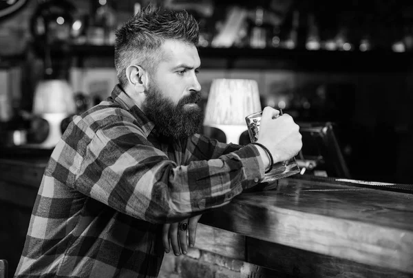 Man met baard doorbrengen vrijetijdsbesteding in de donkere balk. Hipster ontspannen bij bar met bier. Brutale hipster bebaarde man zitten op bar teller drinken bier. Alcohol drinken bestellen Bar is ontspannen plek drankje en te ontspannen — Stockfoto