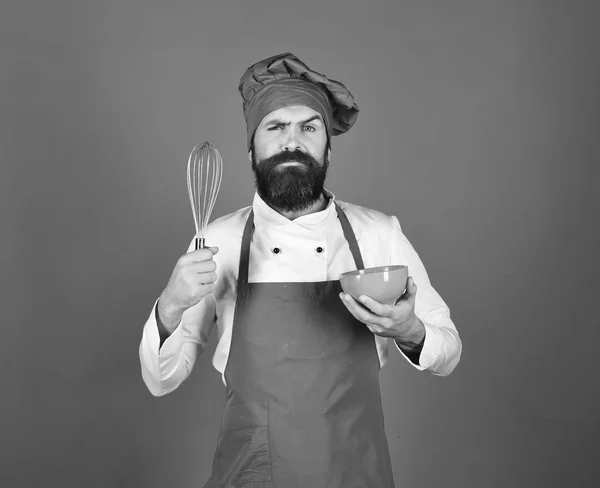 Cocinar con la cara confusa en uniforme de color burdeos utiliza utensilios de cocina —  Fotos de Stock