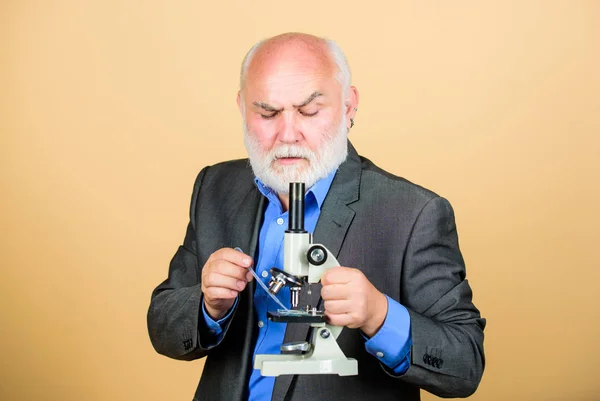 Mature man formal suit with microscope. Doctoral work and postdoctoral employment. Molecular biology PhD projects. Biology experienced lecturer. Professor university lecturer. Scientist microbiology