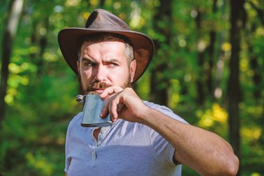 adam hipster sonbahar ormanda dinlenmek. Bahar güneşli hava. kamp ve yürüyüş. acımasız bir görünüm ile olgun erkek metalik şişe alkol içmek. Kovboy şapkalı sakallı adam parkta açık yürüyüş