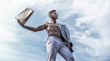 Adam çekici maço taşıma alışveriş çantası kahverengi kağıt yapılmış. Satış sezonu. Bu paketi al. Tezgâhtar kavramı. Adam kas atlet alışveriş çantası gökyüzü arka plan tutun. Sıcak satış ve indirim