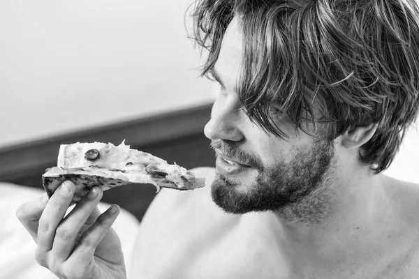 Servicio de reparto de comida. Un hombre sexy come pizza acostado en la cama. Un joven descansando en casa con un desnudo y una pizza. Comer pizza en la cama . — Foto de Stock