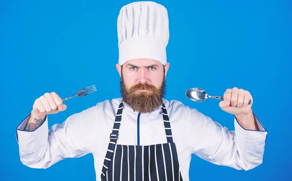 Vamos experimentar o prato. Chef faminto pronto para experimentar comida. Está na hora de provar. Chef sério rosto estrito segurar colher e garfo. Homem bonito com barba segura utensílios de cozinha no fundo azul. Conceito de processo de cozedura — Fotografia de Stock