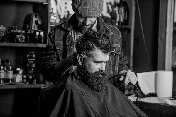 Barber with hair clipper works on haircut of bearded guy barbershop background. Hipster hairstyle concept. Barber with clipper trimming hair on nape of client. Hipster client getting haircut