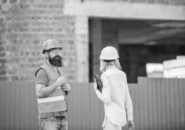Construction site safety inspection. Discuss progress project. Woman inspector and bearded brutal builder discuss construction progress. Construction project inspecting. Safety inspector concept