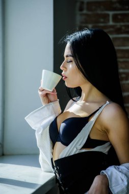 Sabah güneşinin tadını çıkarıyorum. Seksi göğüslü seksi kız pencere kenarında kahve içiyor. Çekici kadın iç çamaşırları evde dinleniyor. Tutkulu gizemli aşık. Kahve zamanı. Ama önce kahve.