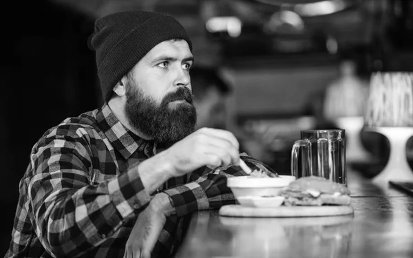 Man with beard eat burger menu. Brutal hipster bearded man sit at bar counter. Cheat meal. High calorie food. Delicious burger concept. Enjoy taste of fresh burger. Hipster hungry man eat burger