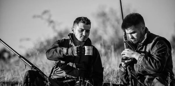 Chasseurs avec des fusils relaxant dans l'environnement naturel. Les amis chasseurs aiment les loisirs. Chasse avec des amis passe-temps loisirs. Les chasseurs satisfaits de la boisson de réchauffement de boisson de capture. Reste pour les hommes réels concept — Photo