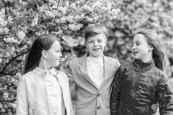 Los niños disfrutan de la primavera. Perdido en flor. Chicas y amigos posando cerca de Sakura. Niños sobre flores rosadas de sakura fondo de árbol. Niños disfrutando de sakura de flor de cerezo. Felices vacaciones de primavera — Foto de Stock