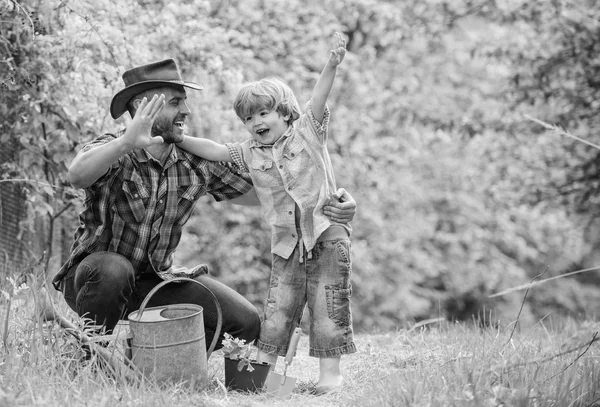 小さな男の子の子供は、農業で父親を助けます。幸せな地球の日。家族の木の看護。エコファーム水やり缶、ポットと蹄。庭の設備。牧場でカウボーイハットをかぶった父と息子。水やりベッド — ストック写真