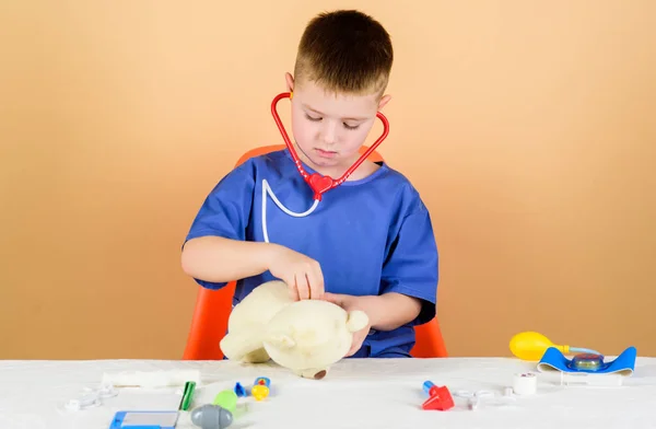 El pequeño doctor está ocupado sentándose en la mesa con herramientas médicas. Examen médico. Concepto de medicina. Procedimientos médicos para el oso de peluche. Niño lindo niño futuro médico carrera. Trabajador del hospital. Asistencia sanitaria — Foto de Stock