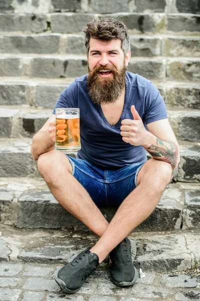 Hipster zrelaksowany picie piwa na zewnątrz. Lekkie piwa lub ciemne Stout pić je wszystkie. Człowiek z brodą i wąsy trzymać piwo ze szkła na zewnątrz. Kawiarnia letni taras. Facet odpoczywać z piwem z zimnego zanurzenia — Zdjęcie stockowe