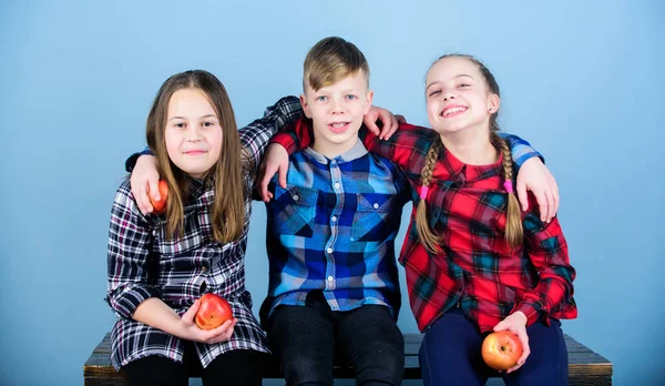 Boy and girls friends in similar checkered clothes eat apple. Teens with healthy snack. Healthy dieting and vitamin nutrition. Eat fruit and be healthy. Friends kids hug each other. Healthy lifestyle