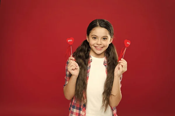 A day when love finds its way. Small girl holding hearts on sticks. Cute girl with small red hearts. Small child with heart shaped decorations. Happy valentines day. The holiday of love and romance