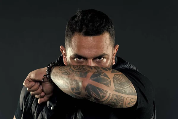 Tattooed elbow hide male face. Tattoo culture concept. Man brutal unshaven hispanic appearance tattooed arm. Bearded man posing with tattoos. Brutal macho with tattoos. Masculinity and brutality