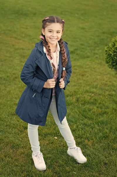 Casaco elegante. Menina bonito rosto trançado cabelo posando casaco no parque de primavera. Roupa para passeios de primavera. Um pequeno modelo de moda. Roupas e acessórios. O miúdo usa casaco de trincheira. Casaco de primavera. Deve ter conceito. — Fotografia de Stock