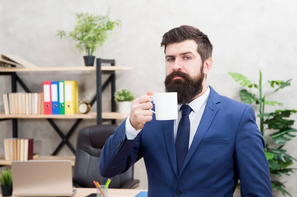 Man bearded businessman hold coffee cup stand office background. Drinking coffee relaxing break. Boss enjoying energy drink. Successful people drink coffee. Caffeine addicted. Start day with coffee