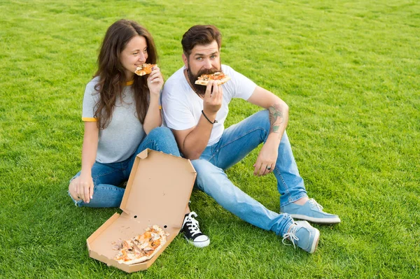 Fast food. Bearded man and woman enjoy cheesy pizza. Couple in love dating outdoors with pizza. Hungry students sharing food. Couple eating pizza relaxing on lawn. Summer picnic easy and quick ideas