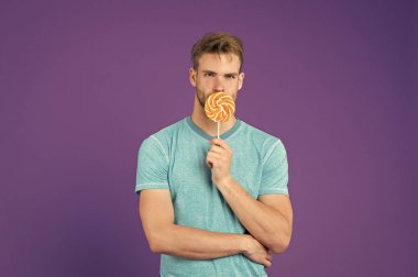 Kıl adamla Lolipop sever. Yemek kavram hile. Şeker sağlık için zararlı. Adam lolipop şeker menekşe arka plan tutun. Adam yakışıklı maço büyük renkli tatlı lolipop yemek. Çocukluk tadına