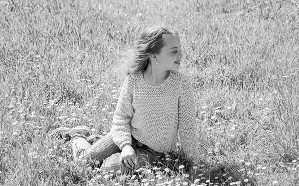 Menina senta-se na grama no gramado, fundo verde. Criança desfrutar de clima ensolarado primavera enquanto sentado no prado. Conceito de primavera. Menina no rosto sorridente passar o lazer ao ar livre — Fotografia de Stock