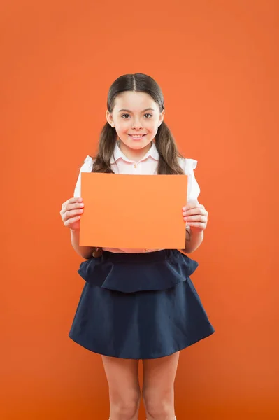 Dikkat lütfen. okul kız turuncu arka plan üzerinde kağıt tutun. kopya alanı. ekle ile okul üniforması mutlu küçük kız. yararlı bilgiler. Okula geri dön. Şuraya bak. notlar yazma. modern eğitim — Stok fotoğraf
