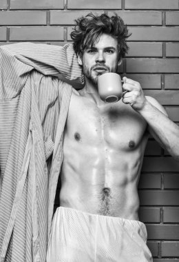 Adam çay veya kahve Kupası tutun. Maço seksi gövde kahve keyfini çıkarın. Atlet uykulu yüz tousled saç giymek bornoz tutun kupa. Sabah kahve kavramı. Sakal içki kahve tuğla duvar arka plan adamla