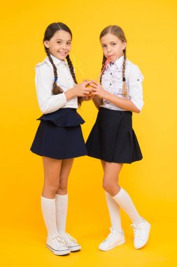 Sağlıklı hissetmek harika. Sarı arka planda susamış okul kızları. Küçük kızlar portakal meyvelerinden meyve suyu içiyor. Sevimli kız bebek doğal içecekler zevk. Sulu snack ile sevimli küçük kızlar