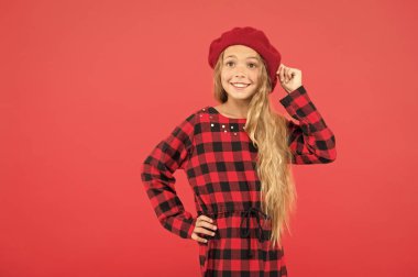 Bere tarzı ilham. Nasıl moda kız gibi bere giymek. Uzun saçlı küçük kız şapka ve kırmızı arka plan üzerinde damalı elbise poz. Kadın için şık bere şapka. Fransız tarzı bere şapka