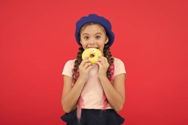 Çocuk gülümseyen kız donut yemeye hazır. Şeker dükkanı ve ekmek kavramı. Pişmiş Donuts büyük fanlar çocuklar. Resist taze yapılmış çörek için imkansız. Kız tutun sırlı tatlı çörek elinde kırmızı arka plan
