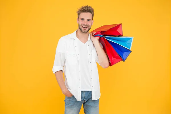 Shopping makes him feel better. Handsome man smiling with shopping bags on yellow background. Happy shopper holding colorful paper bags after shopping. Its fun to go shopping — Stock Photo, Image