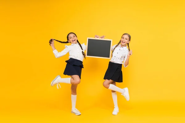 De volta à escola. Crianças felizes segurando quadro-negro da escola em fundo amarelo. Meninas se preparando para a aula. Crianças pequenas sorrindo em uniforme escolar em 1 de setembro, espaço de cópia — Fotografia de Stock
