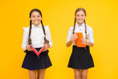 Kız öğrenciler sarı arka planda birlikte çalışma. Eğitim dili. Sevimli çocuklar ders kitabı ile çalışma. Pratik ve okul çalışmaları için okuma becerilerini geliştirmek. Okul konseptine geri dönelim. Kızlar kitap tutun