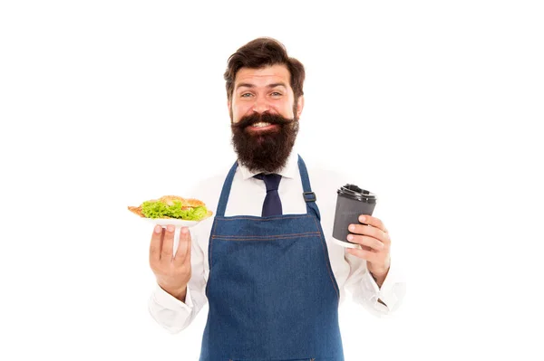 Concepto de Café. Hombre camarero barbudo usar delantal llevar plato con comida y taza de café. Disfruta tu comida. Tipo sirviendo croissant relleno de lechuga y verduras frescas. Comida saludable. Delicioso croissant —  Fotos de Stock