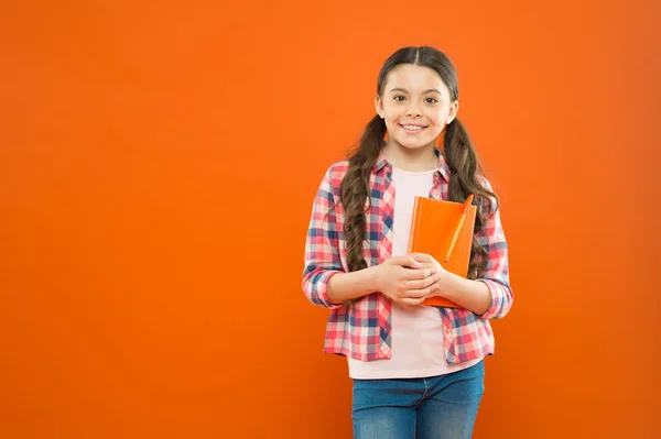 Lição de literatura. de volta à escola. poesia e romance. educação moderna. escola em casa. menina da escola ler livro sobre fundo laranja. Rapariga sorridente com caderno. Escrever nota. Diário infantil. espaço de cópia — Fotografia de Stock